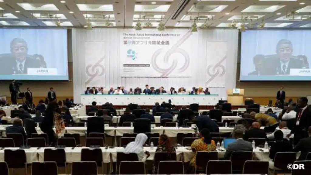 Salle de conférence avec délégués et écrans affichant le représentant japonais lors de la TICAD-9 à Yokohama.