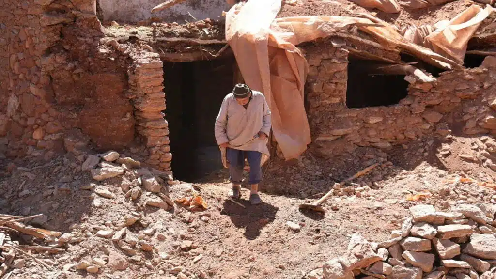 Un homme marche devant une maison en ruine après le séisme d’Al Haouz de septembre 2023, illustrant les destructions qui ont motivé l’augmentation du prélèvement de solidarité contre les catastrophes.