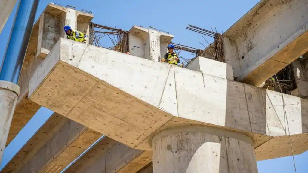 Deux ouvriers en casque et gilet de sécurité travaillent sur les poutres en béton d’un viaduc en construction au port Nador West Med.
